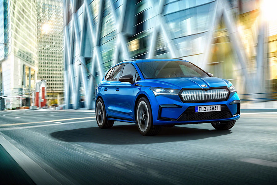 Blauer Škoda fährt dynamisch durch moderne Stadt mit Glasfassaden und urbanem Flair.