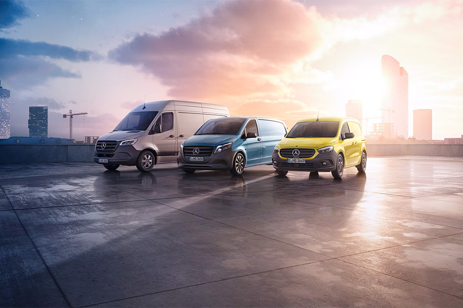 Drei Mercedes-Benz Transporter stehen nebeneinander auf einem urbanen Dachparkplatz bei Sonnenaufgang. Links ein weißer Sprinter, in der Mitte ein blauer Vito und rechts ein gelber Citan, mit moderner Skyline im Hintergrund.