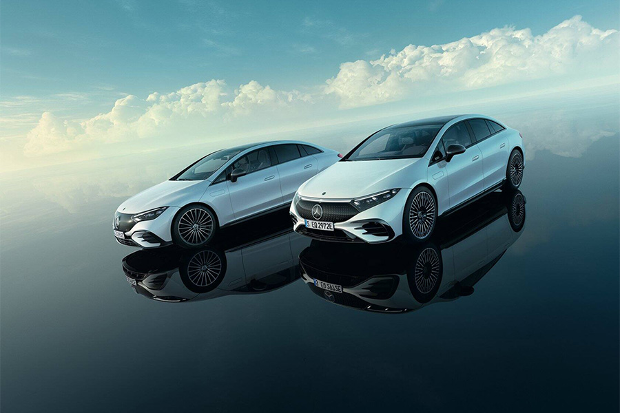 Zwei weiße Mercedes EQ-Modelle spiegeln sich auf glatter Fläche vor dramatischem Himmel.