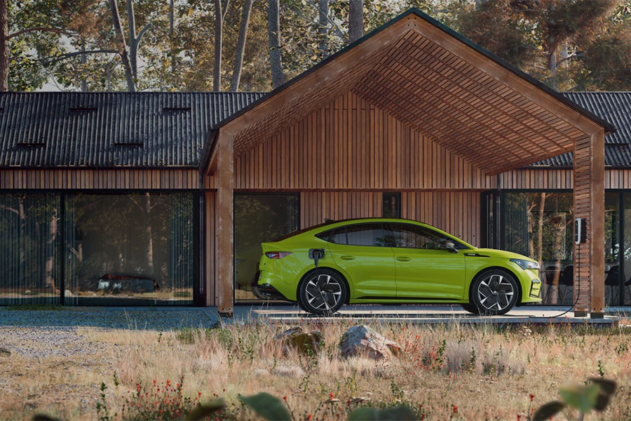 Ein leuchtend grüner Škoda wird unter einem modernen Carport aus Holz an einem Einfamilienhaus im Wald geladen. Die Szene wirkt naturverbunden und nachhaltig, mit Fokus auf Elektromobilität.