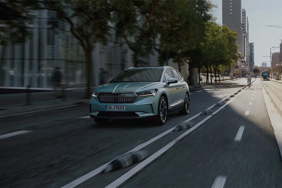 Ein hellblauer Škoda fährt auf einer modernen Stadtstraße mit getrenntem Radweg und Straßenbahntrasse.