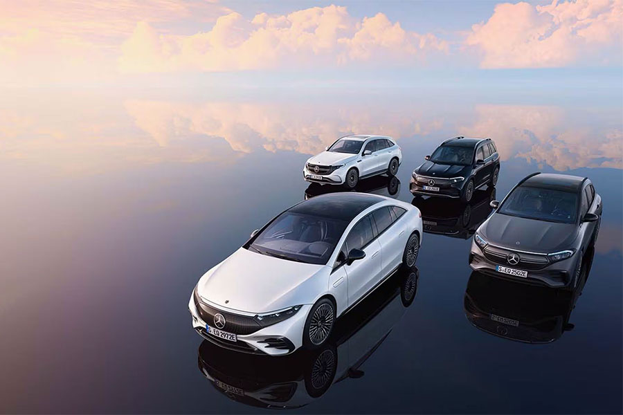 Vier vollelektrische Mercedes-Benz EQ-Modelle stehen auf einer spiegelglatten, surreal wirkenden Fläche unter einem Himmel mit weichen rosa Wolken – im Vordergrund der EQS, daneben der EQA, hinten links der EQB und daneben der EQC.