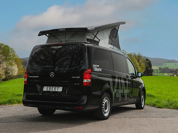 Ein schwarzer Mercedes-Benz Vito 119 CDI mit Aufstelldach steht am Straßenrand vor einer grünen Wiese und hügeliger Landschaft. Das Fahrzeug trägt die Beschriftung ‚CAMPSTAR BY PÖSSL GROUP‘ und ‚AUTOWELT EBERT‘.