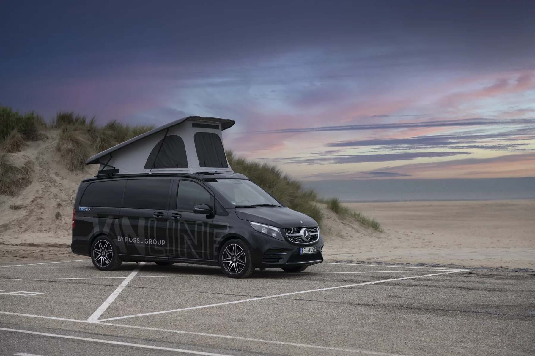 Schwarzer Mercedes-Benz Campervan mit aufgeklapptem Schlafdach steht bei Sonnenuntergang auf einem Parkplatz an den Dünen eines Strandes.