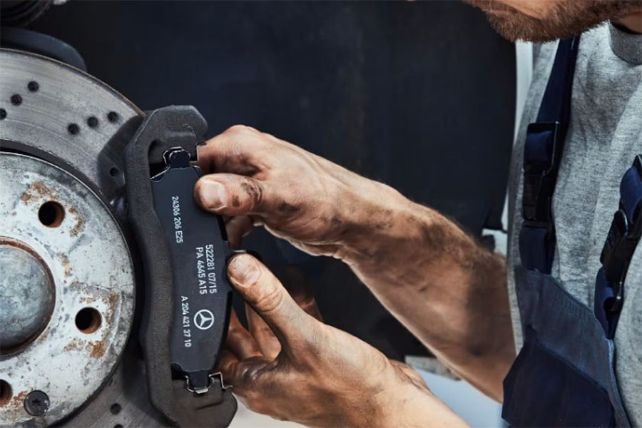 Mechaniker mit schmutzigen Händen montiert originale Mercedes-Benz Bremsbeläge an eine Bremsscheibe.