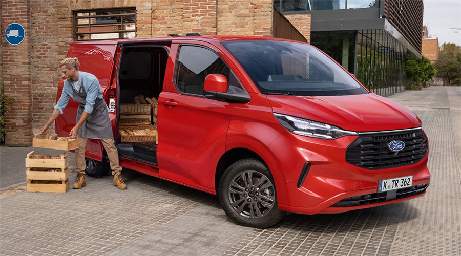 Bäcker entlädt frisches Brot aus einem roten Ford Transit Custom vor einer modernen Bäckerei – ideale Lösung für Handwerk und Lieferdienste.