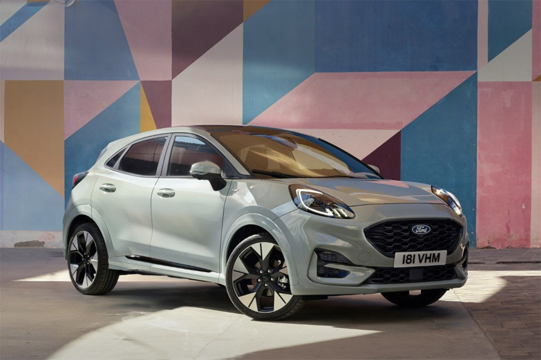 Ford Puma in heller Lackierung vor bunter Wand mit geometrischen Mustern – stilvolle Präsentation in urbaner Umgebung.