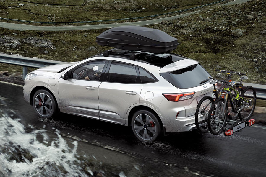 Ein silberner Ford Kuga fährt auf einer kurvigen Bergstraße, ausgestattet mit Dachbox und Fahrradträger – ideal für aktive Outdoor-Abenteuer und Familienreisen.