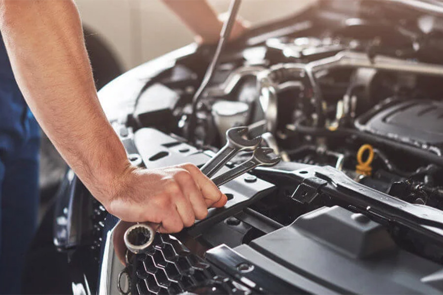 Mechaniker lehnt sich über einen geöffneten Motorraum und hält mehrere Schraubenschlüssel in der Hand.
