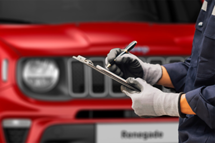 Kfz-Mitarbeiter mit Handschuhen schreibt auf ein Klemmbrett vor einem roten SUV mit markanter Front und Rundscheinwerfern.