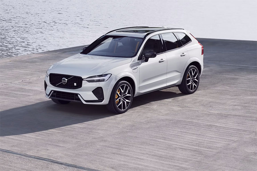 Weißer Volvo SUV steht auf einer Betonfläche am Wasser. Das Fahrzeug ist schräg von vorne fotografiert und verfügt über schwarze Felgen und ein Panoramadach.
