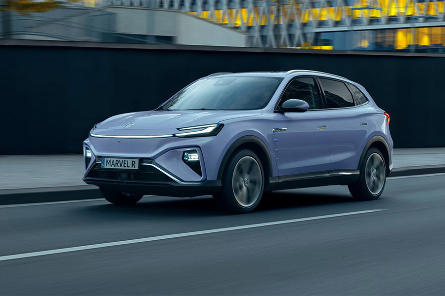 Hellvioletter MG SUV fährt auf einer städtischen Straße entlang einer modernen Gebäudefassade mit beleuchteten Fenstern.