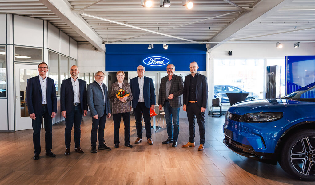 7 Personen stehen in einem Ford Autohaus, eine Frau hält einen Blumenstrauß in der Hand.