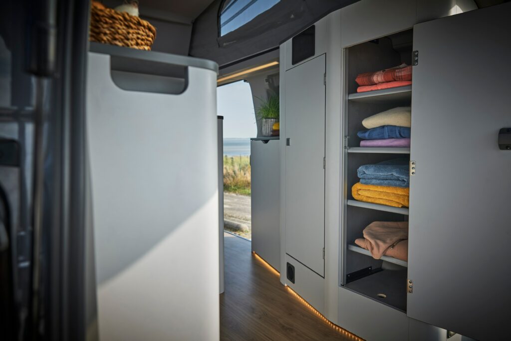 Im Innenraum von einem Ford Transit Nugget mit einem geöffneten Kleiderschrank.