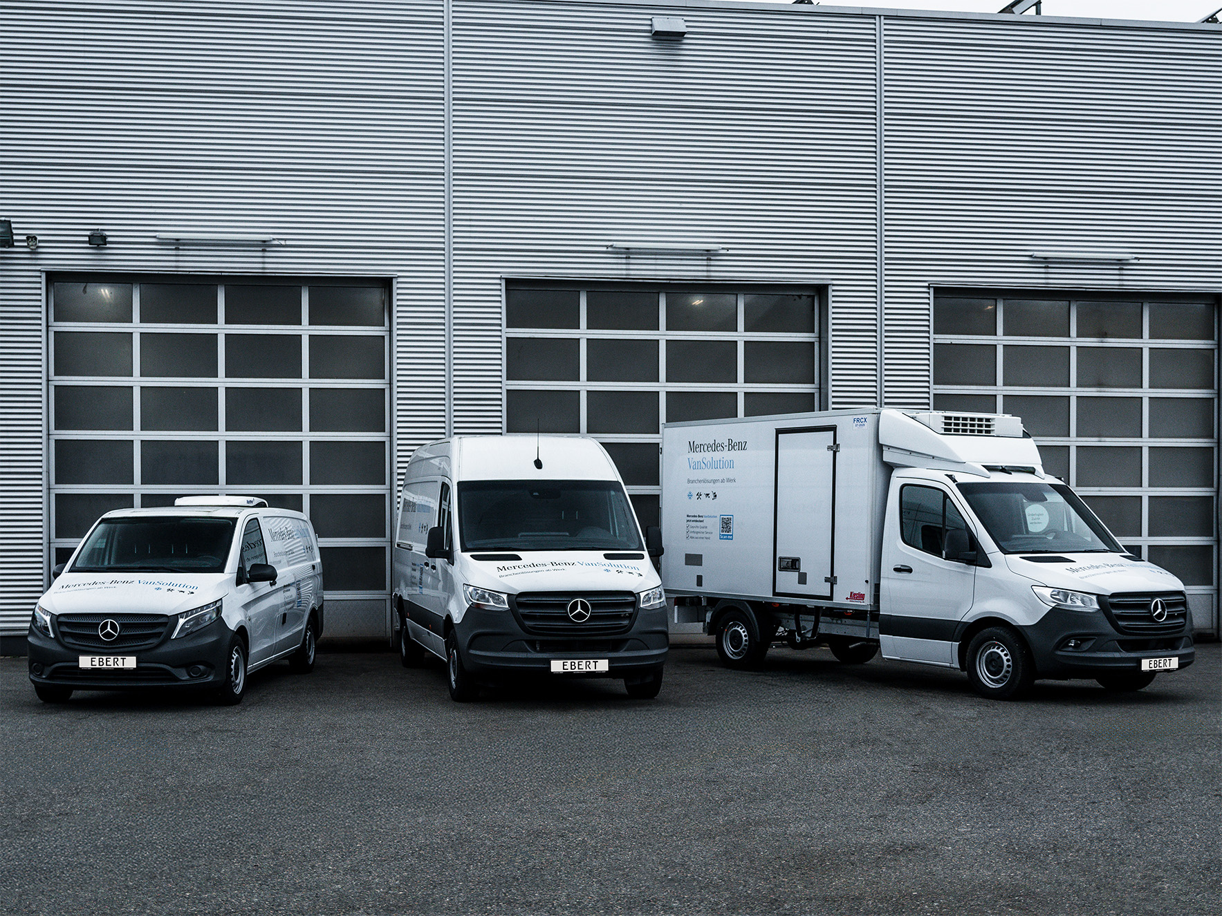 Drei weiße Mercedes-Benz Transporter mit der Aufschrift „VanSolution“ stehen nebeneinander auf einem Hof vor einer Werkstatthalle.