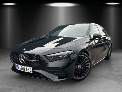 Front- und Seitenansicht eines schwarzen Mercedes-Benz Kompaktwagens in einem Studioumfeld mit Spotlights. Fahrzeug mit Diamantgrill, LED-Scheinwerfern, AMG-Line Frontschürze und schwarzen mehrspeichigen Leichtmetallrädern.