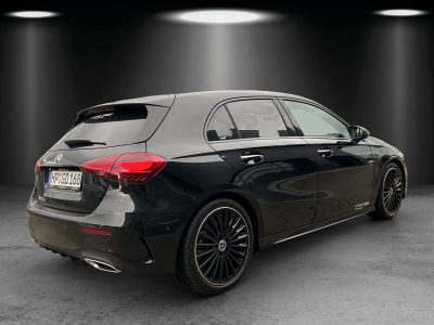 Heck- und Seitenansicht eines schwarzen Mercedes-Benz Kompaktwagens in einem Studio-Setup mit Spotbeleuchtung. Ausgestattet mit AMG-Line Exterieur, getönten Scheiben, zweiflutiger Endrohranlage und schwarzen mehrspeichigen Leichtmetallrädern.