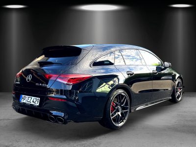 Rückansicht eines schwarzen Mercedes-AMG CLA 45 S Shooting Brake mit vierflutiger Abgasanlage, getönten Scheiben, schwarzen Leichtmetallfelgen und roten Bremssätteln. Das Fahrzeug steht in einem Studio-Setup mit Spotbeleuchtung auf grauem Boden.