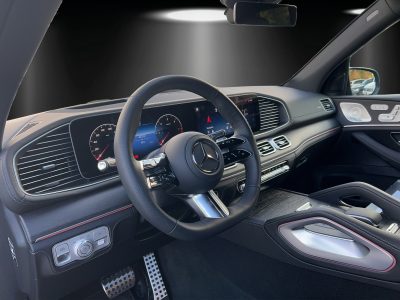 Innenraum eines Mercedes-AMG mit Blick auf das schwarze Multifunktionslenkrad, volldigitales Cockpit, Navigationsdisplay, Aluminium-Akzente, Ambientebeleuchtung und sportliches Armaturenbrett mit roten Kontrastnähten – modern und hochwertig gestaltet.